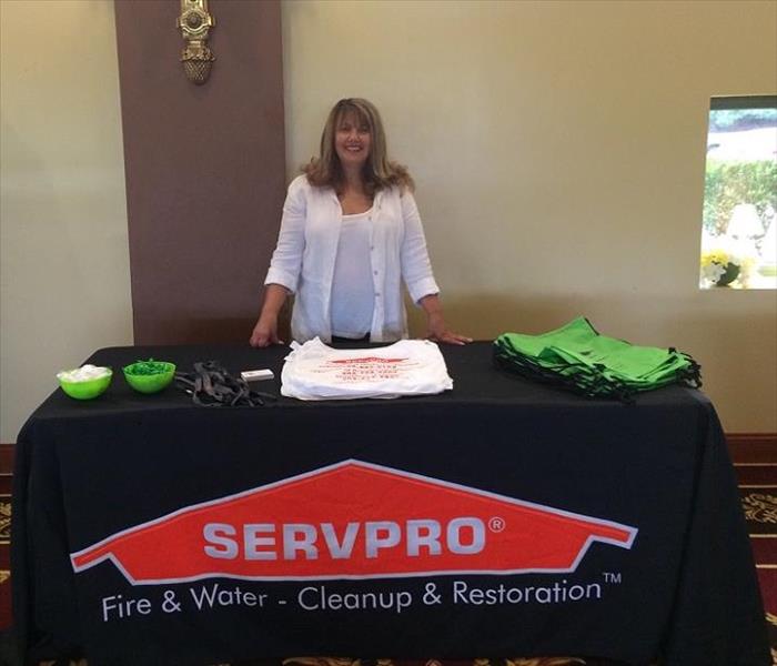 Lady standing behind table with SERVPRO tablecloth.  Giveaways on top of table